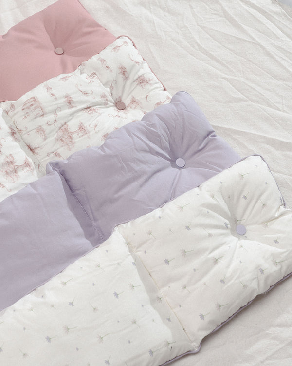 A collection of soft and cozy Soycraft carrier cushions in pastel shades of pink, lavender, and white, featuring delicate patterns and tufted buttons for added comfort and style. Perfect for enhancing your pet's travel experience.